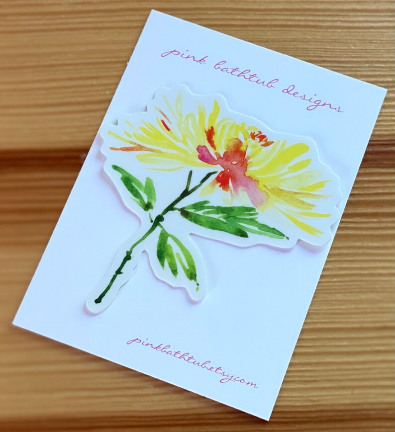 以下が含まれることがあります： ピンクの中心を持つ黄色の花の水彩画。花は、「ピンクバスタブデザイン」と「pinkbathtubetsy.com」というピンクのテキストが書かれた白いカードの上にあります。