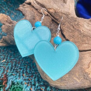 Può includere: Un paio di orecchini a forma di cuore color turchese con ganci d'argento e perline turchesi. Gli orecchini sono realizzati in un materiale traslucido con una finitura scintillante.