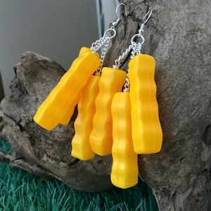 Può includere: Un paio di orecchini pendenti gialli con una catena d'argento. Gli orecchini sono composti da più pezzi gialli che sono collegati tra loro.