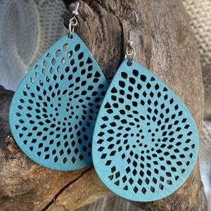 Può includere: Un paio di orecchini a goccia turchese con un design a spirale traforata. Gli orecchini in legno hanno ganci per orecchie color argento. Esposti su un pezzo di legno trasportato dalle correnti.