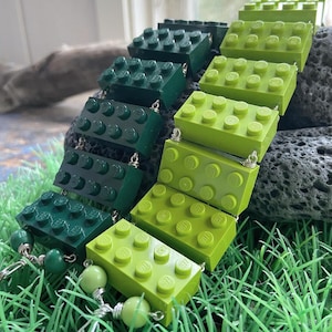 Può includere: Un braccialetto di Lego verde e verde lime con filo d'argento e perline verdi. Il braccialetto è su un letto di erba verde.