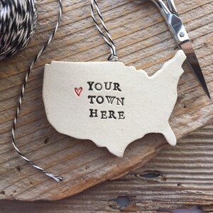 May include: White ceramic ornament shaped like the United States with a red heart and the text "YOUR TOWN HERE" in black.