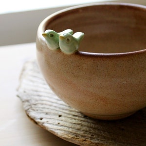 May include: A brown ceramic bowl with two small green bird figurines on the rim.