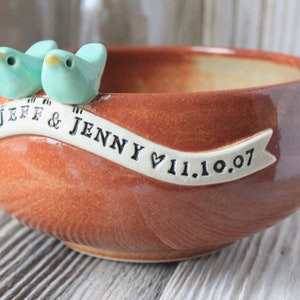May include: A brown ceramic bowl with two light blue birds perched on the rim. A white banner with the text "JEFF & JENNY &hearts; 11.10.07" is wrapped around the bowl.