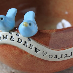 May include: A brown ceramic bowl with two blue birds perched on the rim. The bowl has a white banner with the text "SAM & DREW &hearts; 08.12.17" inscribed on it.