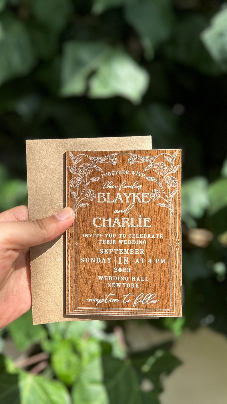 Pu&ograve; includere: Invito di nozze in legno con dettagli floreali e i nomi di Blayke e Charlie. L'invito include la data, l'ora e il luogo del matrimonio. Una busta di carta kraft &egrave; dietro l'invito.