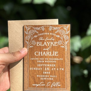 Pu&ograve; includere: Un invito di nozze in legno con decorazioni floreali e i nomi Blayke e Charlie. L'invito include la data, l'ora e il luogo del matrimonio a New York.