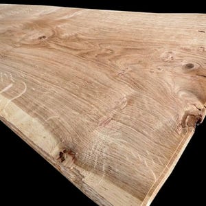 Può includere: Una grande lastra di legno marrone chiaro con un bordo vivo. Il legno presenta una venatura naturale e una superficie liscia.