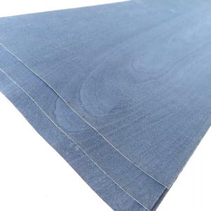 Pode incluir: Três folhas de folheado de madeira azul-acinzentado sobrepostas, mostrando os padrões naturais do grão. A madeira tem um acabamento liso e fosco. As folhas estão ligeiramente anguladas, revelando suas bordas e as sutis variações de cor e textura.