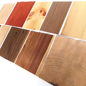 Op de afbeelding: Assortiment van houtfineerstalen in verschillende kleuren en houtnerfpatronen. De stalen zijn in een verspringend patroon gerangschikt, wat de natuurlijke schoonheid van hout laat zien.