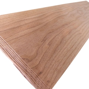 Op de afbeelding: Een stapel onafgewerkte houten planken. De planken zijn lichtbruin van kleur met zichtbare houtnerfpatronen. De randen van de planken zijn gelaagd en tonen de verschillende houtlagen. Het hout lijkt glad en klaar om afgewerkt te worden.