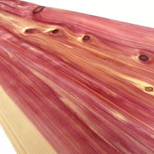 Peut inclure: Gros plan sur une pièce de bois de couleur rouge-violet avec des motifs de grain visibles. Le bois présente des nœuds et des stries plus claires, jaunâtres, créant un aspect naturel et texturé. Le bois est probablement du cèdre.