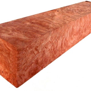 Può includere: Un blocco rettangolare di legno rosso con un motivo a spirale. Il legno è di colore marrone rossiccio chiaro con striature più scure.