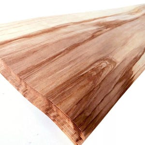 Puede incluir: Una pila de finas láminas de madera marrón claro, con vetas de color marrón más oscuro. La madera tiene un aspecto natural, sin terminar, con texturas y variaciones de color visibles. Las láminas están cuidadosamente apiladas, lo que sugiere que están listas para un proyecto de carpintería.