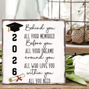 May include: A graduation-themed wooden sign with a black mortarboard, the year 2026, and a scroll. The sign features the text "Behind you, all your memories. Before you, all your dreams. Around you, all who love you. Within you, all you need."