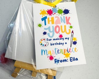 May include: A gift set for a birthday party, including a small canvas, wooden easel, and a tag that says "Thank You" with colorful paint splatters. The tag also reads "For making my birthday a masterpiece From: Ella."