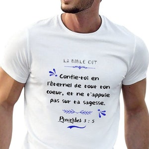 Peut inclure: T-shirt blanc avec l'inscription "LA BIBLE DIT" et un verset biblique en français. Le texte bleu est orné de motifs floraux. Le t-shirt est de style col rond.