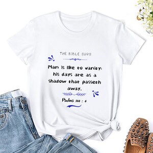 Peut inclure: T-shirt blanc avec une citation bleue de la Bible : « La Bible dit L'homme est semblable à la vanité : ses jours sont comme une ombre qui passe. Psaumes 144 : 4 »