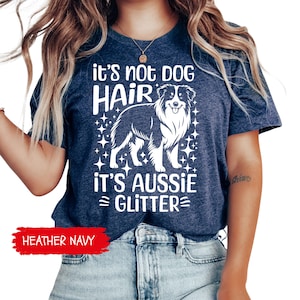 May include: Heather navy t-shirt with the text "it's not DOG HAIR it's AUSSIE GLITTER" in white. The design includes a detailed illustration of an Australian Shepherd dog. The shirt is a casual wear item.