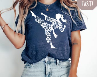 May include: Heather navy blue t-shirt featuring a white floral design of a person in a karate stance. The shirt has a crew neck and short sleeves. The words "Ship Fast!" are in a light brown box.
