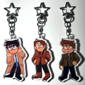 May include: Three acrylic keychains featuring cartoon illustrations of characters. Each keychain has a silver star-shaped clasp and a chain. The characters are depicted in various outfits, with one wearing a tan coat and blue tie, another in a brown jacket, and the third in a green jacket.
