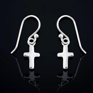 May include: A pair of silver-colored cross earrings. Each earring features a small, polished cross pendant suspended from a curved ear wire. The earrings are displayed against a black background, with a reflective surface.