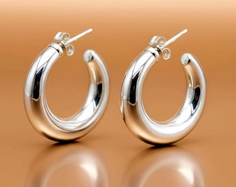 May include: A pair of polished silver hoop earrings with a thick, rounded profile. Each earring features a smooth, reflective surface and a secure post-back closure mechanism, showcasing a clean, circular design that catches the light.