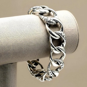 May include: A silver chain link bracelet featuring alternating smooth polished links and textured links with a raised dot pattern. The bracelet is constructed from thick, interlocking metal loops that create a substantial and continuous circular design.
