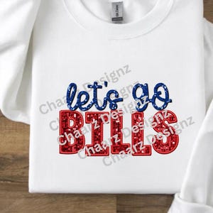 May include: White long-sleeve sweatshirt with the text "let's go BILLS" in blue and red glitter lettering. The sweatshirt is made of a soft material and is perfect for game day or casual wear.