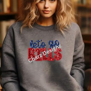 May include: A gray sweatshirt with the text "let's go BILLS" in red and blue glitter lettering. The sweatshirt also has the text "Charz Designz" in white. The sweatshirt is a crew neck style.