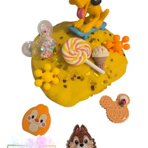 May include: A yellow playdough scene featuring a Pluto figurine on a blue skateboard, a Mickey Mouse-shaped shaker filled with glitter, and various Disney-themed embellishments. Includes a lollipop, ice cream cone, and Chip and Dale figures.