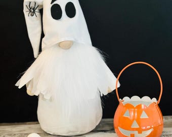 May include: A white ghost gnome with a black spider on its hat, holding a small orange pumpkin-shaped bucket with a white face.