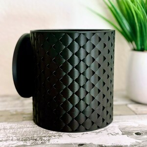 May include: A black ceramic mug with a textured diamond pattern. The mug has a matching lid.