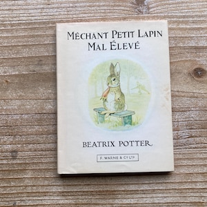 May include: A vintage children's book titled "Méchant Petit Lapin Mal Élevé" by Beatrix Potter. The cover features an illustration of a brown rabbit sitting on a wooden bench, holding a carrot.