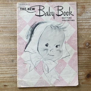 May include: Vintage "The New Baby Book" with a baby illustration on the cover. The cover has a pink and white diamond pattern. The book is for knitting and crocheting. The price is 10 cents.