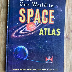 May include: A vintage "Our World in Space Atlas" book by Hammond's. The cover features a vibrant illustration of planets, galaxies, and the word "SPACE" in large, yellow letters. The book contains 70 pages with 50 world and space maps.