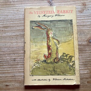 May include: A vintage hardcover book titled The Velveteen Rabbit by Margery Williams with illustrations by William Nicholson. The cover features a tan background with a central illustration of a brown rabbit standing in a grassy field.