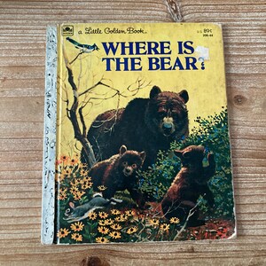 May include: A vintage Little Golden Book titled "Where Is The Bear?" features a yellow cover with a bear illustration. The cover art depicts a large bear with two cubs, a rabbit, and the title in blue text. The book is set against a backdrop of yellow flowers.