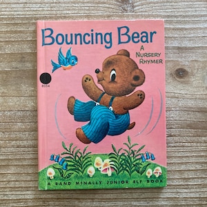 May include: Vintage children's book titled "Bouncing Bear" with a pink cover. The cover features a cartoon bear in blue overalls, a blue bird, and the text "A Nursery Rhyme". The book is a Rand McNally Junior Elf Book.
