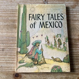 May include: Vintage book titled "Fairy Tales of Mexico" with a colorful illustration. The cover art depicts a man in a sombrero, a large cactus, and other figures. The book is set against a light background.