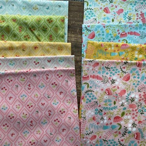 Op de afbeelding: Een verzameling stoffen met bloempatronen in verschillende kleuren. De stoffen hebben ontwerpen van bloemen, vlinders en geometrische vormen in tinten roze, geel, groen en blauw. De stoffen zijn naast elkaar gerangschikt.