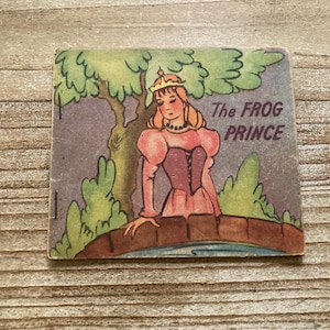 May include: Vintage illustration of a princess from "The Frog Prince" fairy tale. The princess is depicted in a pink dress and gold crown, standing on a bridge. The image has a vintage aesthetic with the title text at the top.
