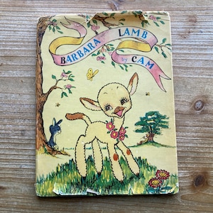 May include: Vintage children's book cover featuring a cartoon lamb with a floral necklace. The title "Barbara Lamb" is displayed on a yellow banner, with illustrations of a tree, flowers, and a rabbit. The book is by Cam.
