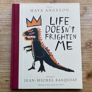 May include: A hardcover book titled "Life Doesn't Frighten Me" by Maya Angelou, with paintings by Jean-Michel Basquiat. The cover features a black dinosaur-like figure with a crown and the book's title in large black letters.