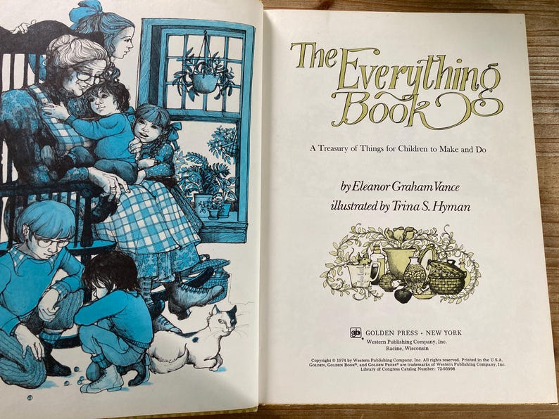 May include: Open book with illustrations and text. The left page features a blue-toned illustration of a family scene with children and a cat. The right page displays the title "The Everything Book" and author information.