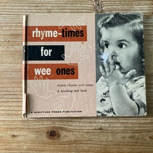 Peut inclure: Livre pour enfants vintage intitulé "rhyme-times for wee ones". La couverture présente le titre en rouge et noir, avec des illustrations de mains. Une photo en noir et blanc d'un bébé est à droite. Le livre est un outil pédagogique avec des comptines et des chansons.
