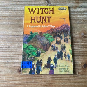 May include: A paperback book titled "Witch Hunt: It Happened in Salem Village" with a colorful illustration of people in period clothing. The cover features a yellow sky and a crowd of people walking towards a gallows.