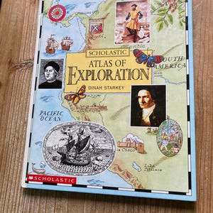 May include: A hardcover book titled "Scholastic Atlas of Exploration" by Dinah Starkey. The cover features a map with illustrations of ships, explorers, and butterflies, with a light blue border and the Scholastic logo.