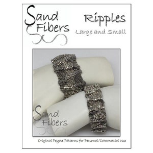 May include: Two silver beaded bracelets with a rippled pattern. The bracelets are displayed on white stands. The image includes the text "Sand Fibers" and "Ripples Large and Small".