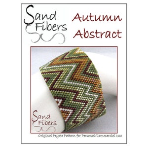 Puede incluir: Un brazalete de cuentas verde, marrón y dorado con un patrón de chevron. El brazalete está etiquetado como "Sand Fibers Autumn Abstract".